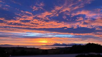 A sunset over a coastal landscape with a clear sky and distant mountains.
