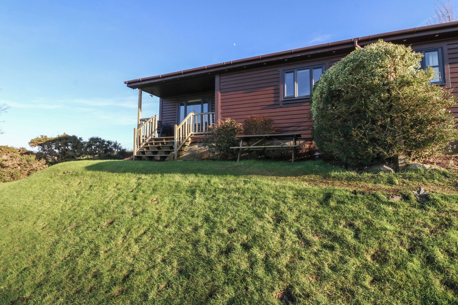 A two-story house with a front porch, a small garden, and a grassy hill.
