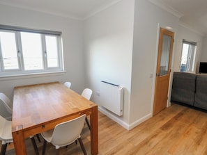 Una habitación con una mesa de comedor de madera, sillas blancas, un radiador, un sofá gris y una puerta de madera.