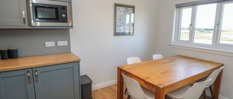 A modern kitchen with grey cabinets, a built-in microwave, and a wooden dining table with four chairs.