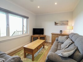 Una sala de estar con un sofá, una mesa de centro de madera, un televisor sobre un mueble, una lámpara y un cuadro en la pared.