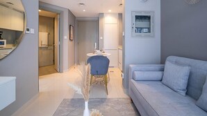 Una sala de estar moderna con un sofá gris, un comedor con una mesa redonda y sillas, y un baño visible a través de un puerta abierta.