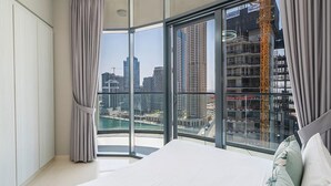 Un dormitorio con una cama grande, vistas a un paisaje urbano y un balcón con puerta de vidrio.