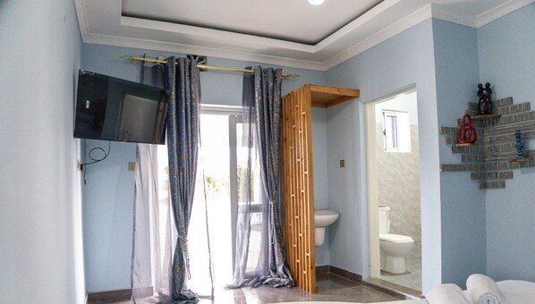 Ein Badezimmer mit Toilette, einer Duschkabine und einem an der Wand befestigten Fernseher.