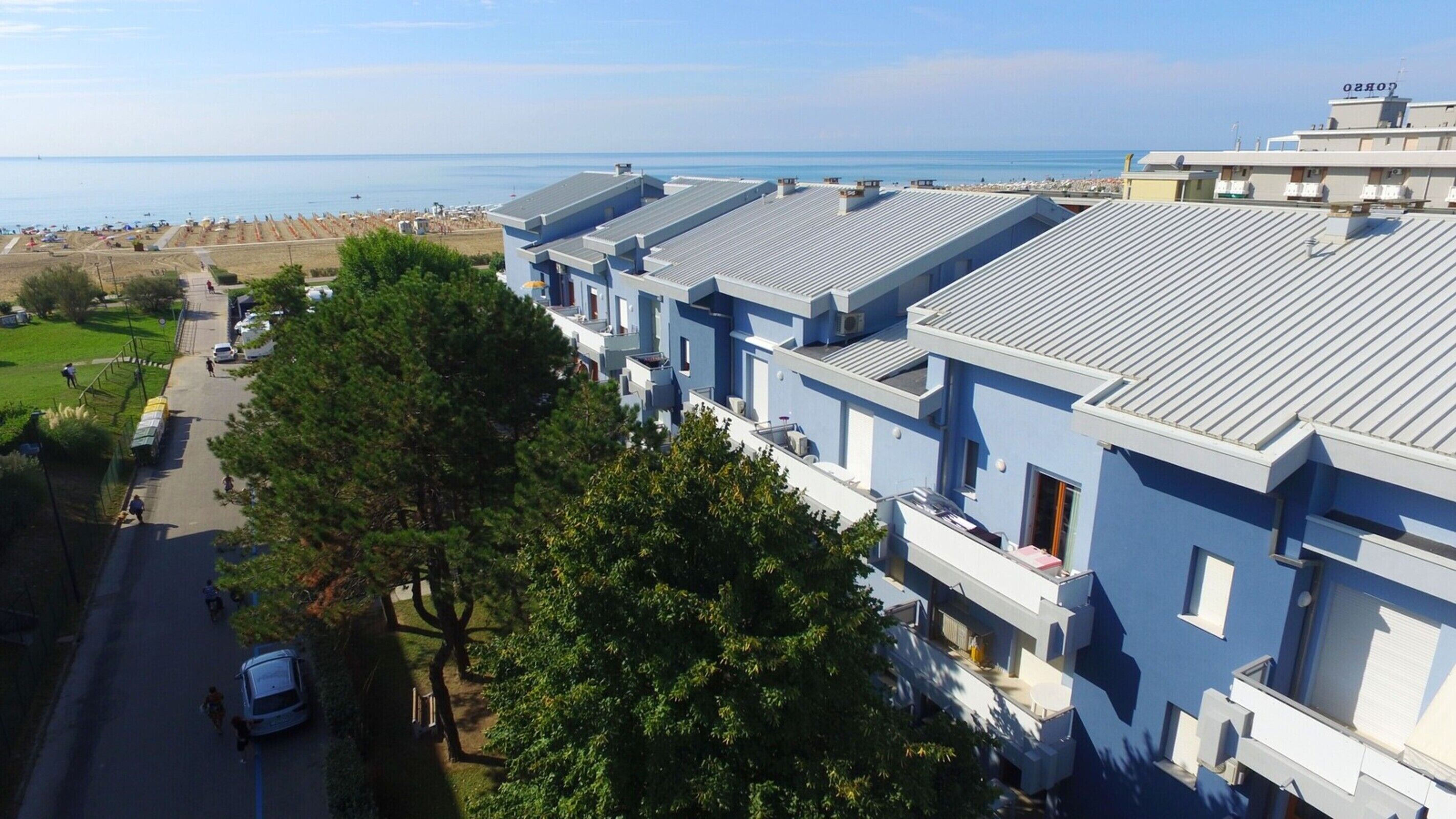 Eine Reihe moderner, hellblauer Gebäude mit flachen Dächern, vermutlich Teil eines Hotels oder Resorts, direkt neben einem Strand mit freiem Blick auf das Meer.