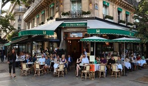 An outdoor cafe with tables and chairs, a green awning, and a sign reading "Les Deux Magots". - A PERFECT PARISIAN RETREAT IN THE HEART OF SAINT-GERMAIN- RUE PAUL LOUIS COURIER (Paris)