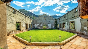 A courtyard with a central lawn, stone walls, and a mountain backdrop.