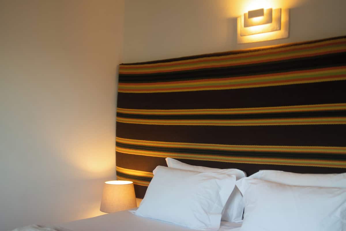 A neatly made bed with white linens and folded towels, a bedside lamp, and a striped headboard.