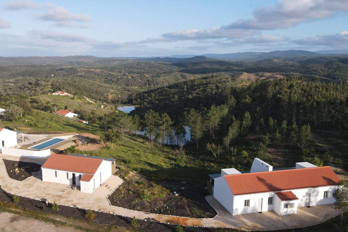 A residential area with white houses and red roofs, surrounded by hills and a lake.