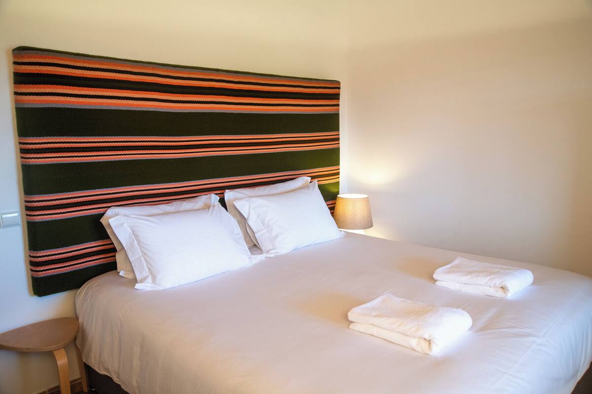 A neatly made bed with white linens, a striped headboard, and two folded towels on the bed.