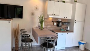 A compact kitchen with white cabinets, a wooden countertop, a built-in oven, and a small dining area with stools. - Apartments Valentinovo (Novi Vinodolski)