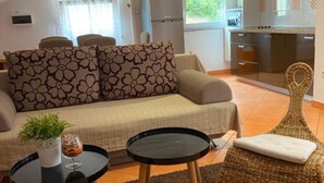 A compact living space with a sofa, two small tables, a woven chair, and a kitchenette. - Apartments Lara Rab (Rab)