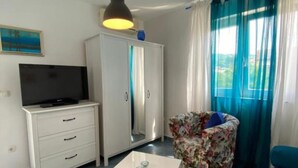A room with a TV on a white cabinet, a floral chair, a white table, and a wardrobe with a mirror. - Apartments Lara Rab (Rab)