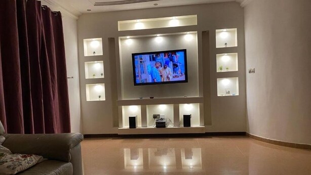 A living room with a flat-screen TV mounted on a wall, surrounded by recessed lighting. - The Manor. (Lomé)