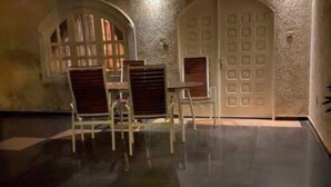 A room with a tiled floor, two wooden chairs, a small table, and a door with a window. - The Manor. (Lomé)