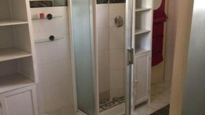A bathroom with a glass shower enclosure, white tiled walls, and a red towel hanging on the wall. - The Manor. (Lomé)