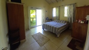 A bedroom with a bed, a ceiling fan, a sliding glass door leading to a balcony, and a small table with a chair.