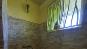 A bathroom with stone-patterned walls, a window with blinds, and a shower area with a towel rack.