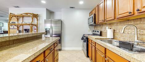 A kitchen with wooden cabinets, granite countertops, stainless steel appliances, and a tiled backsplash.