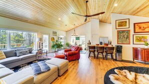 A spacious living area with a wooden ceiling, a large sofa, a red armchair, and a dining table with chairs. - Hot Tub, Deck & Fire Pit: Chic Louisville Home! (Louisville)