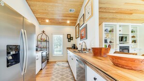 A modern kitchen with wooden flooring, a stainless steel refrigerator, white cabinets, and a wooden countertop. - Hot Tub, Deck & Fire Pit: Chic Louisville Home! (Louisville)
