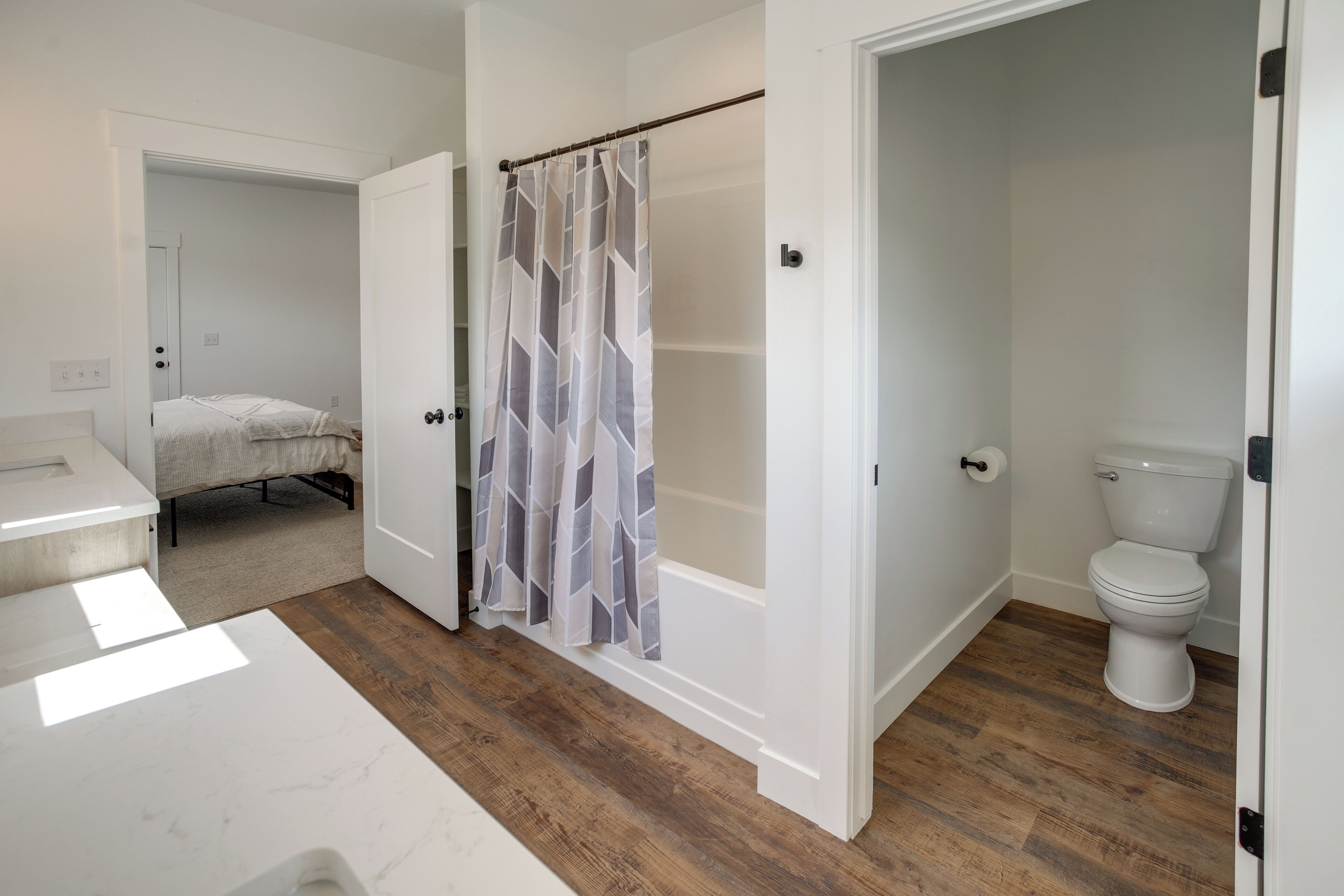 Un baño con cortina de ducha, inodoro y una cama en la habitación contigua.
