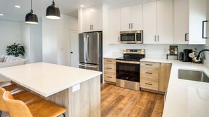 A modern kitchen with white cabinets, stainless steel appliances, and a wooden floor.