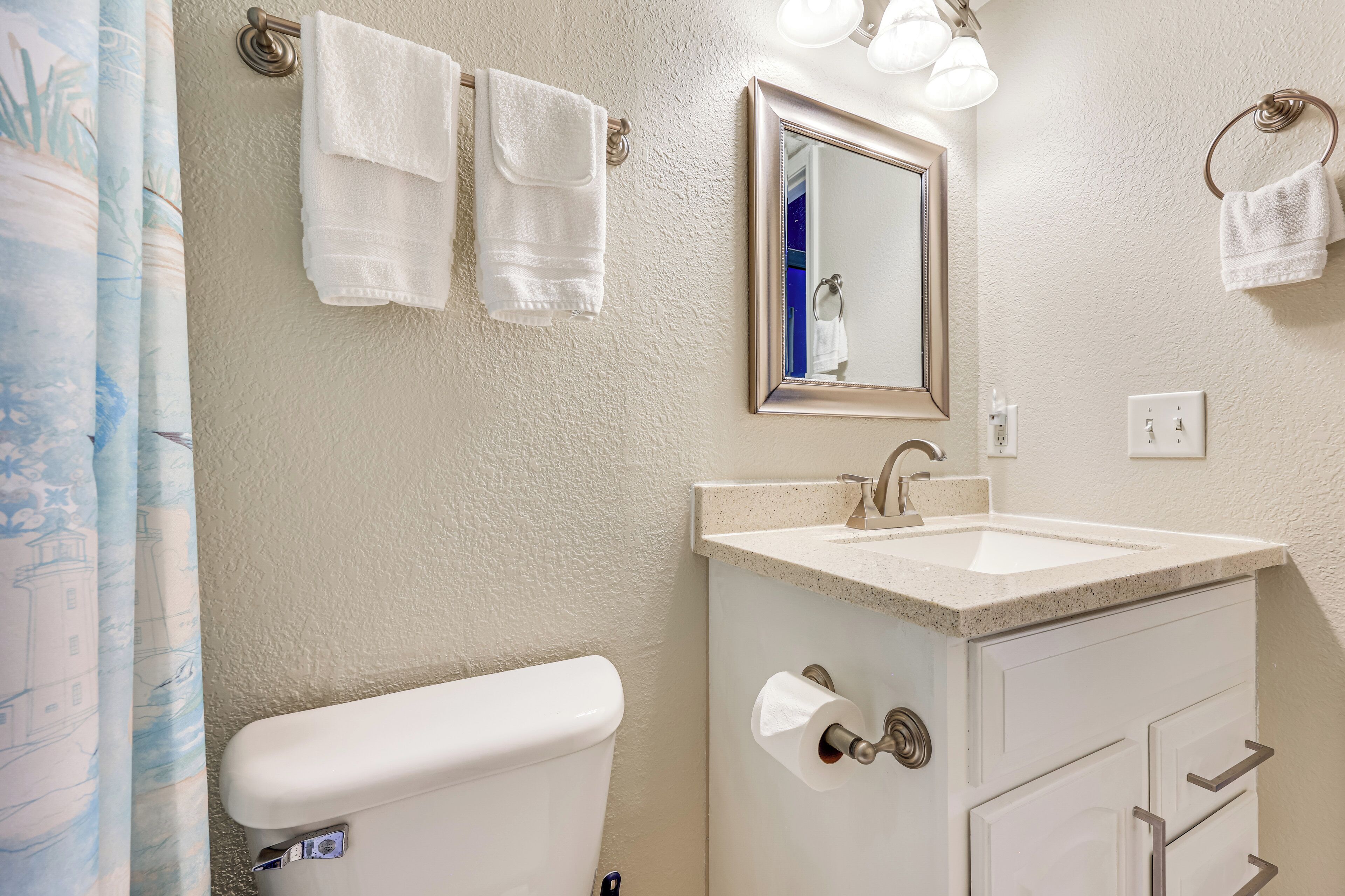 Un bagno con WC, lavandino e specchio. Due asciugamani sono appesi a ganci.