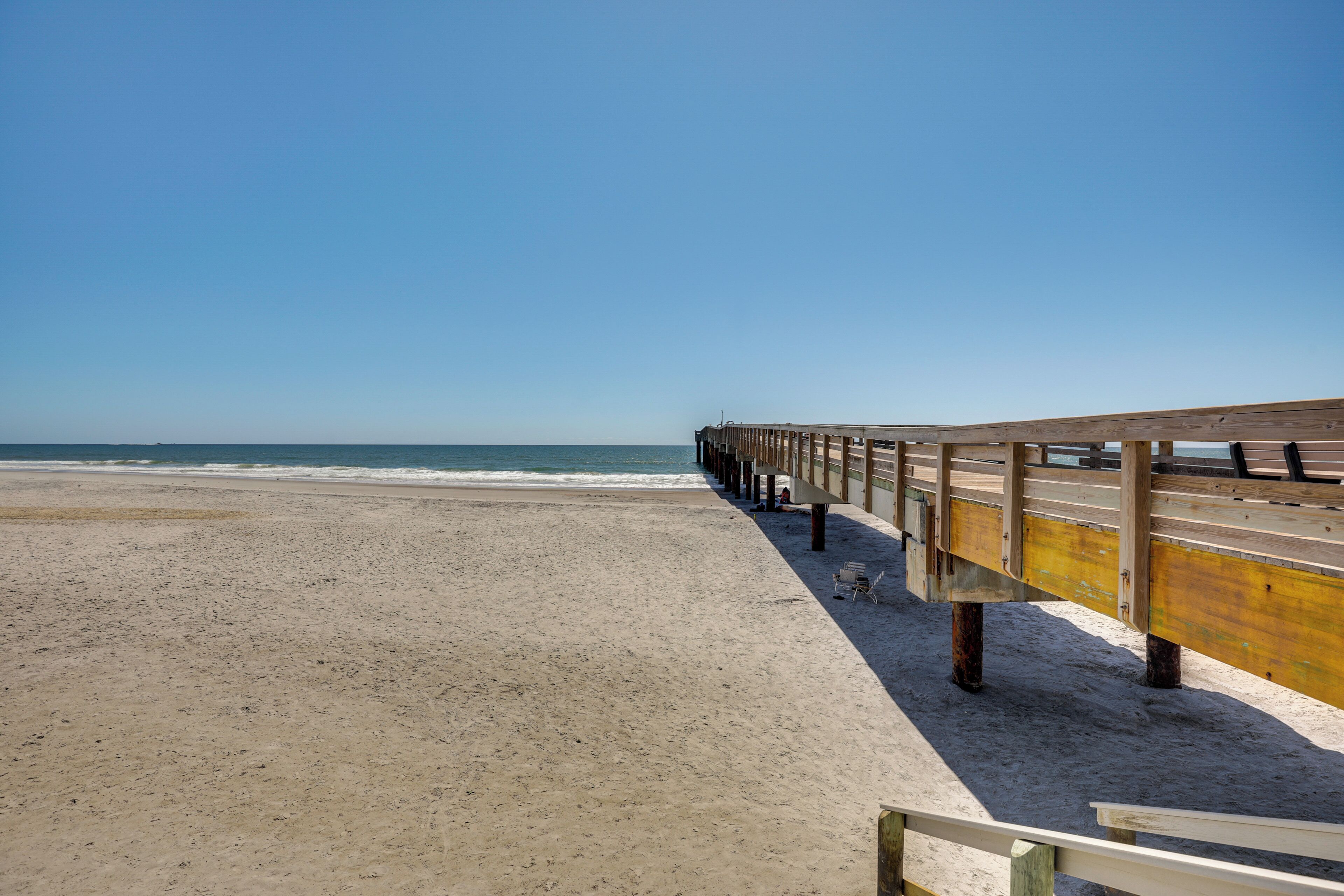Une plage avec une jetée en bois qui s’avance dans l’océan.