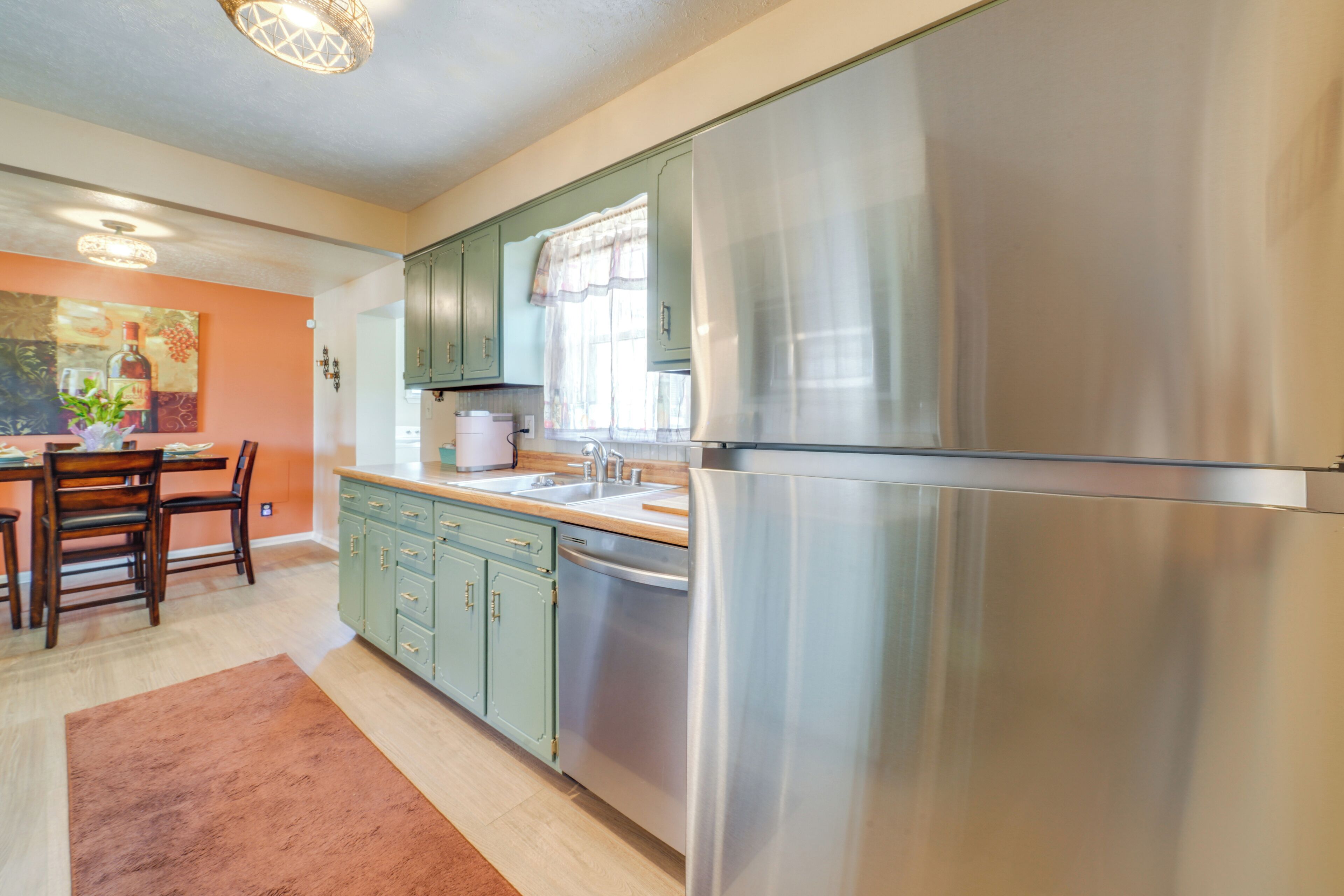 Una cucina moderna con elettrodomestici in acciaio inossidabile, pensili verdi e un'area pranzo con sedie e tavolo in legno.