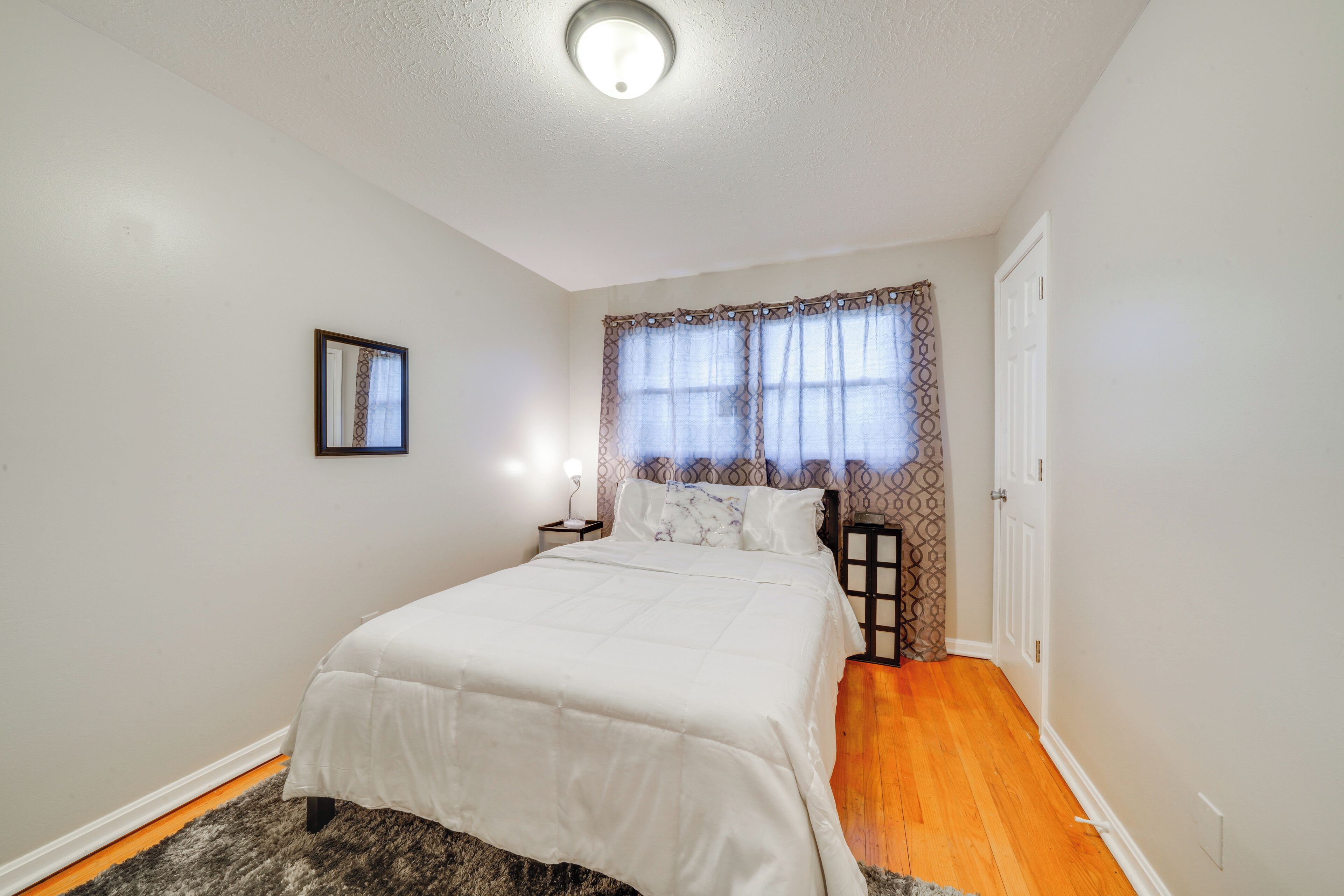 Un dormitorio con cama, mesita de noche, ventana con cortinas y puerta.