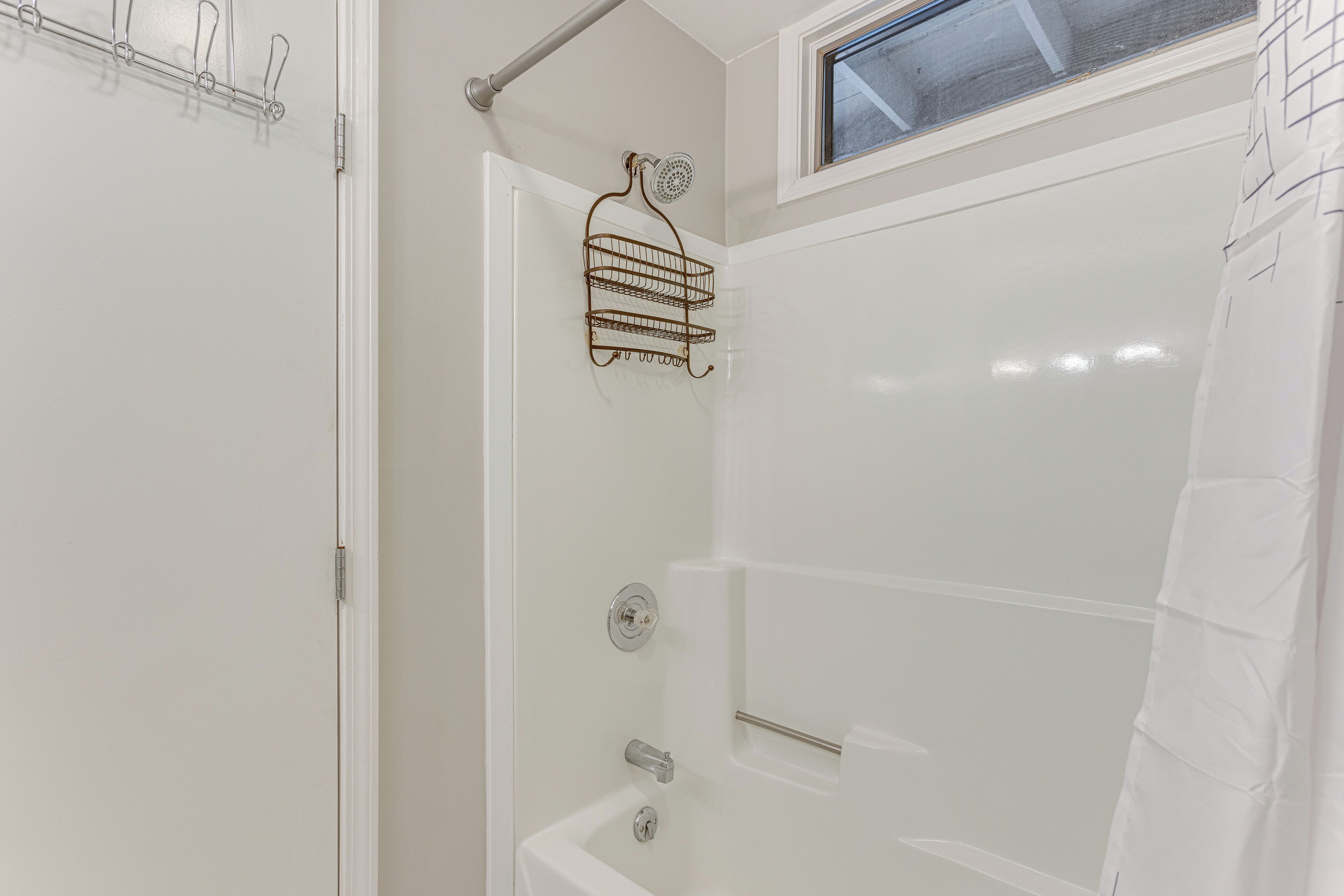 A shower with a glass door, a metal rack, and a window above.