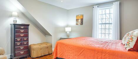 Une chambre à coucher comprenant un lit, une commode, une table de chevet, une lampe, une fenêtre avec des rideaux et un ventilateur de plafond.