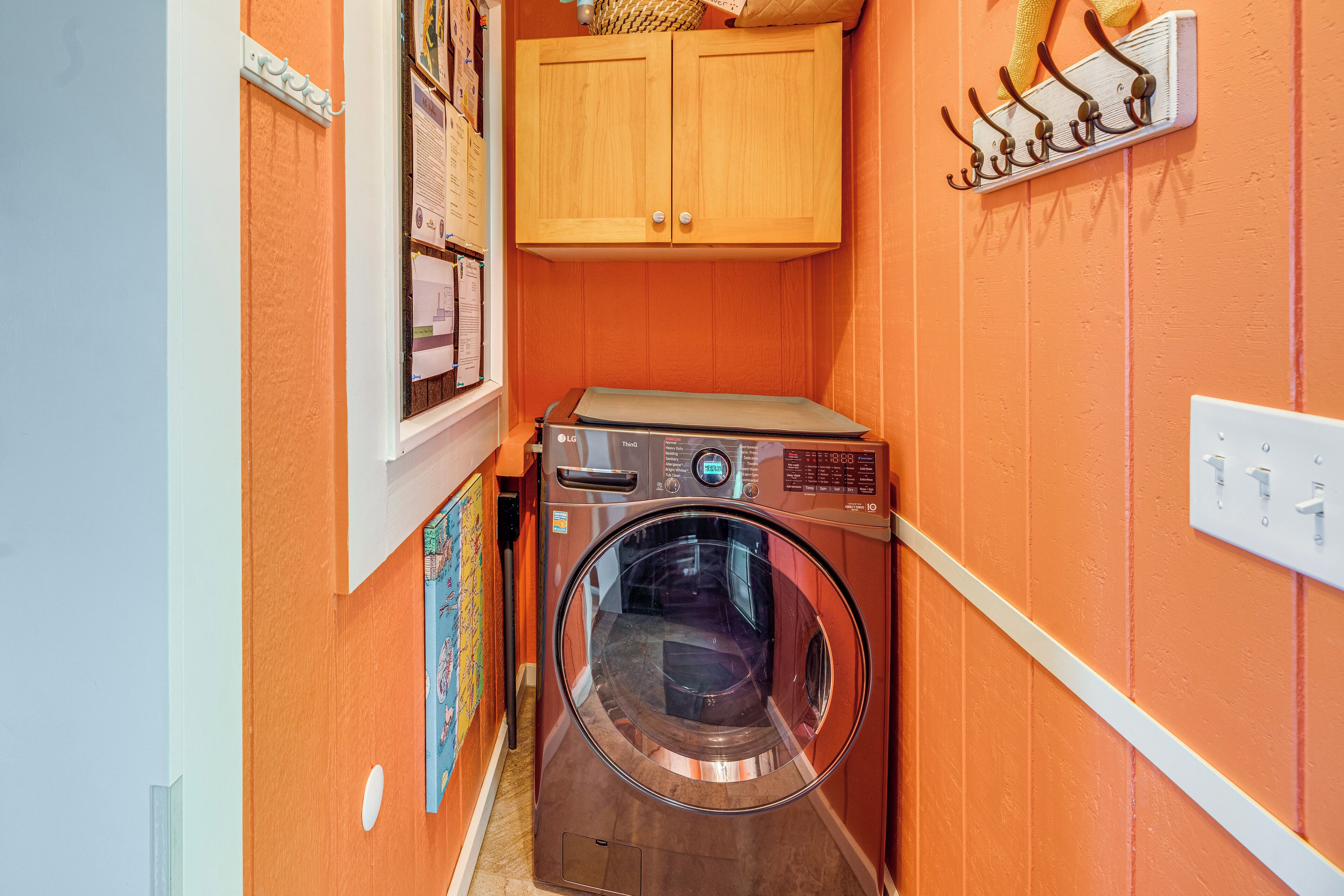 A compact laundry room with a washing machine, a cabinet above it, and a wall-mounted hook rack.