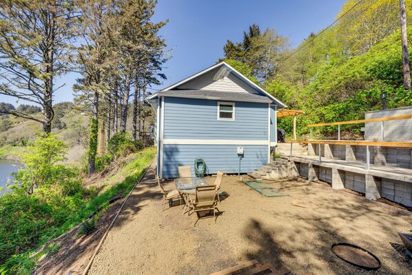 A blue house with a patio area, a table with chairs, and a view of a lake. - Walk to Winema Road Beach: Home w/ Hot Tub! (Neskowin)