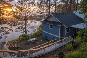 A blue house with a deck overlooking a lake, surrounded by trees. - Walk to Winema Road Beach: Home w/ Hot Tub! (Neskowin)