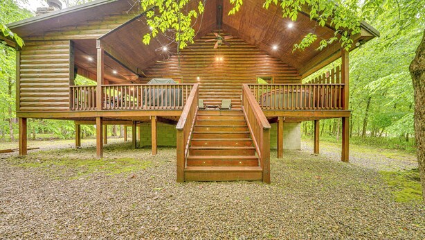 A wooden cabin with a central staircase, a balcony on each side, and a gravel ground.