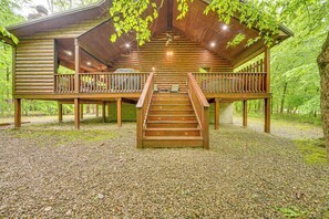 A wooden cabin with a central staircase, a balcony on each side, and a gravel ground. - Private Hot Tub & Deck: Woodsy Broken Bow Retreat (Broken Bow)