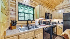 A wooden cabin-style kitchen with a double sink, stove, microwave, and refrigerator.