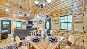 A wooden interior with a dining table set for four, a fireplace, and a large window.