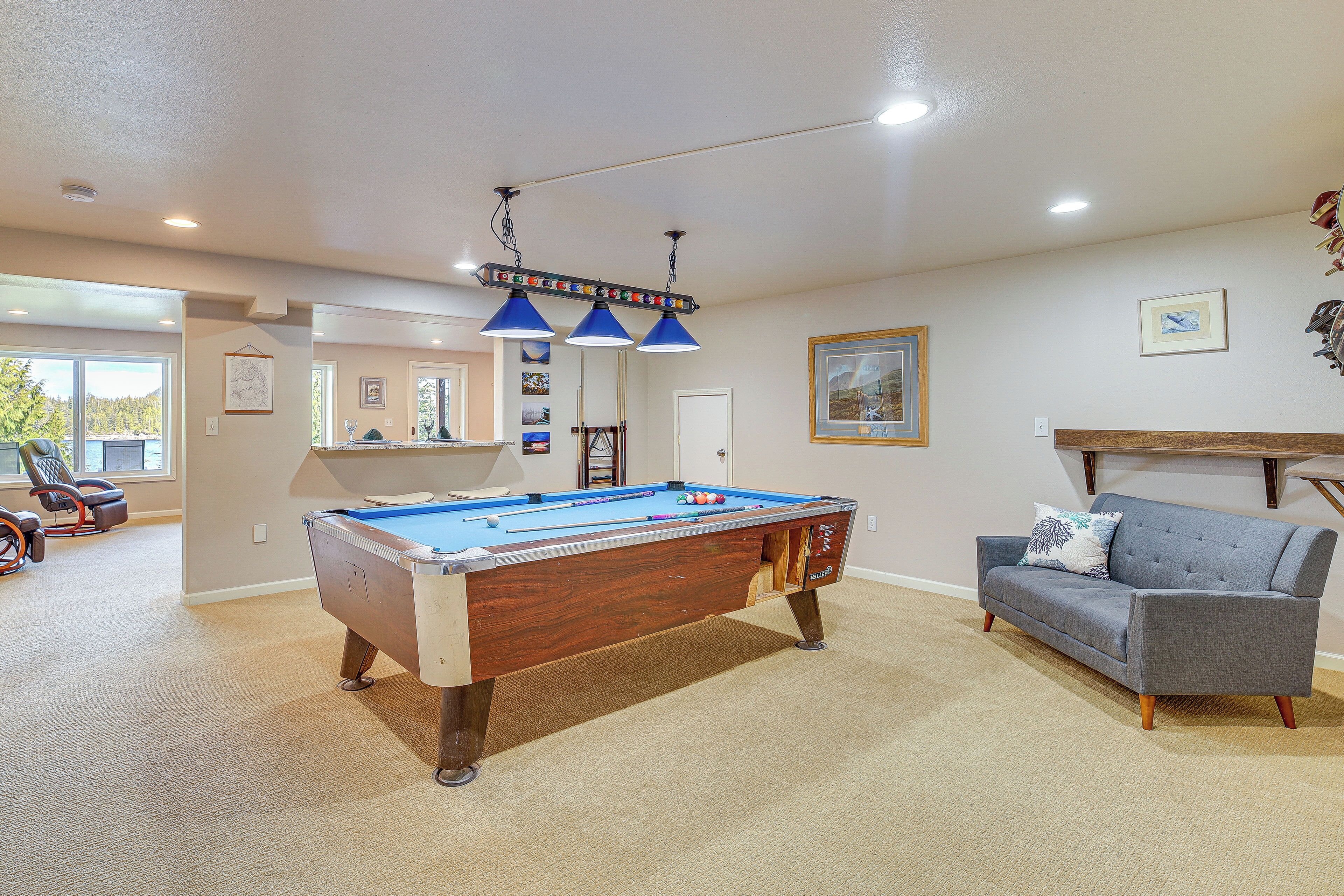 Une table de billard dans une pièce où se trouvent un canapé gris et un banc en bois.