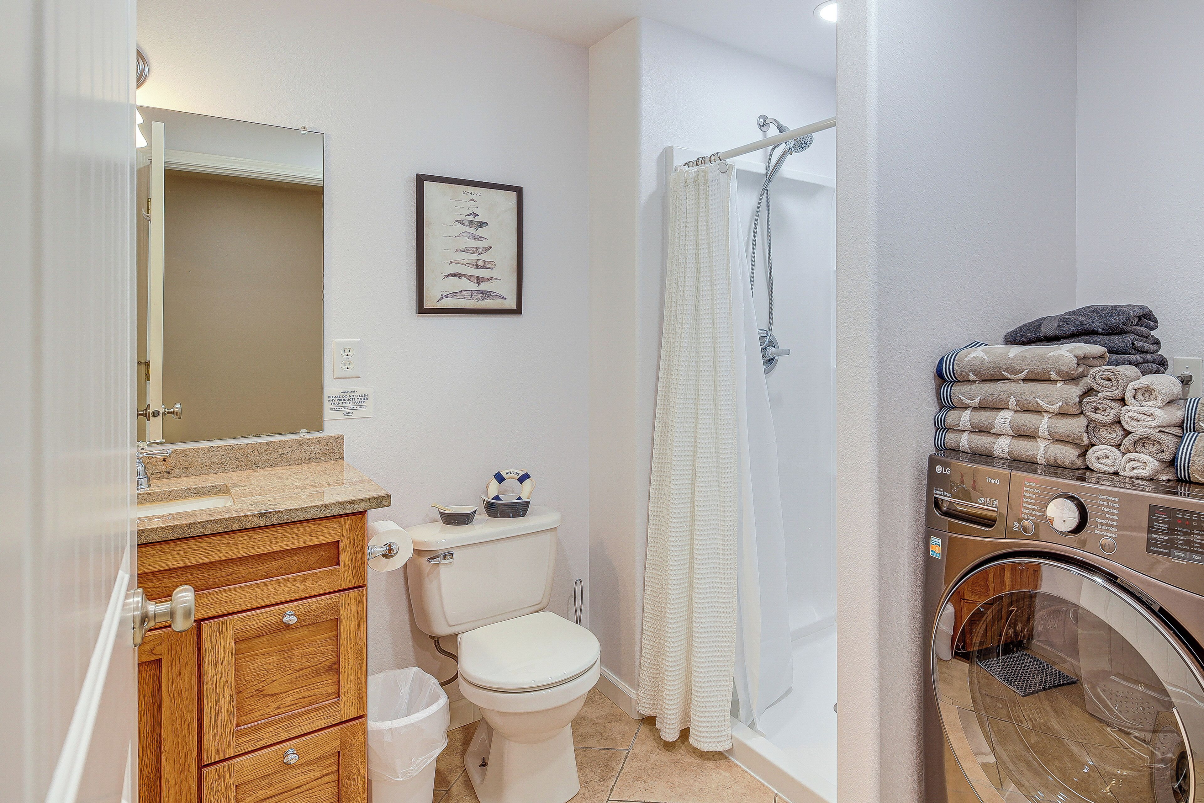 A bathroom with a toilet, sink, mirror, shower curtain, and a stacked laundry basket.