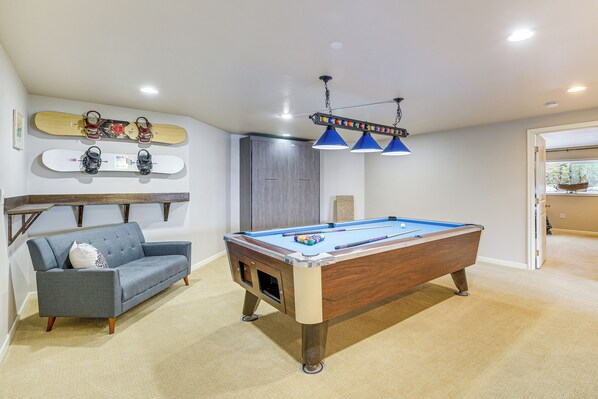 A pool table in a room with a gray sofa, a ceiling-mounted light fixture, and a skateboard on the wall. - Fish & Hike: Apartment w/ Pool Table in Ketchikan! (Ketchikan)
