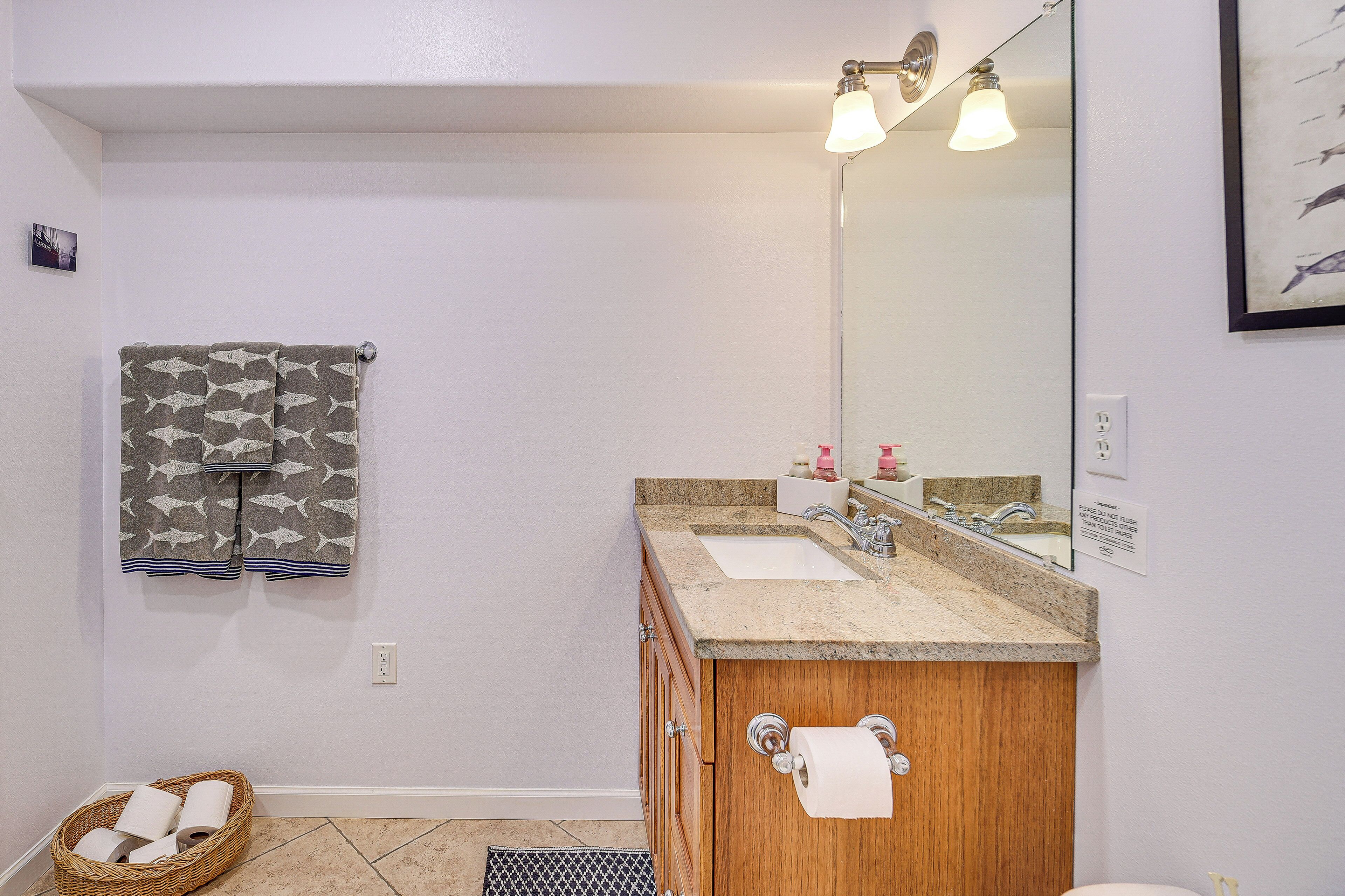 Une salle de bain avec un meuble-lavabo en bois, deux vasques, un grand miroir et un porte-serviettes orné d’une serviette à motifs.