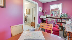 A room with a wooden table, a red chair, and a map on the table. There is a bookshelf filled with books and decorative items.