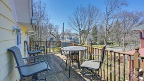 A wooden deck with outdoor furniture, including chairs and a table, overlooking a residential area with houses and trees.