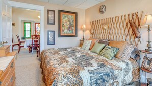 A bedroom with a large bed, a wooden headboard, a dining table with chairs, and a door with a green frame.