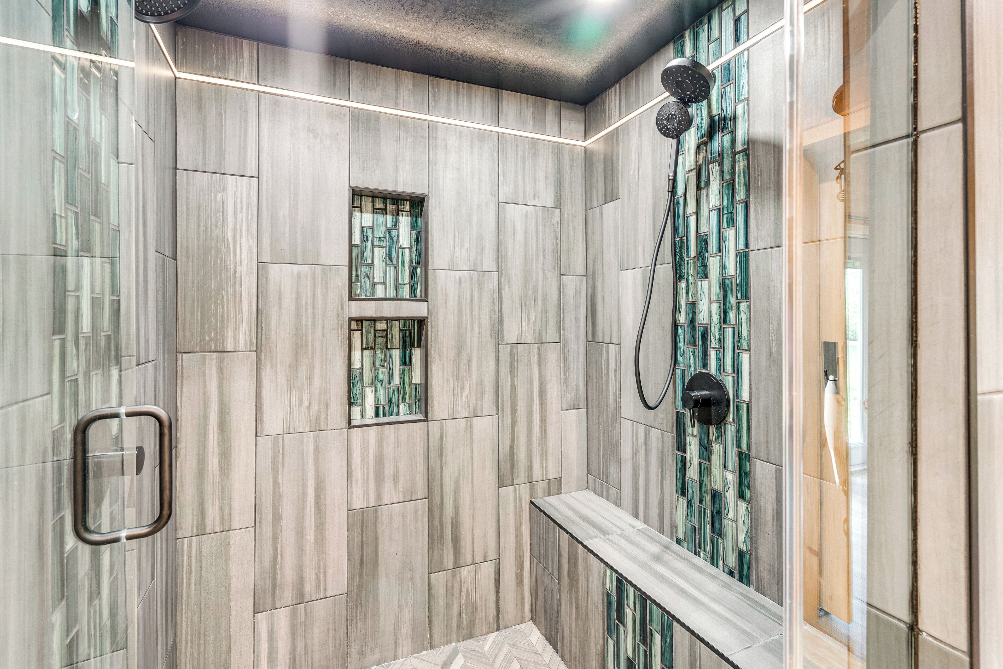 A modern shower area with a bench, a glass-enclosed window, and a showerhead.