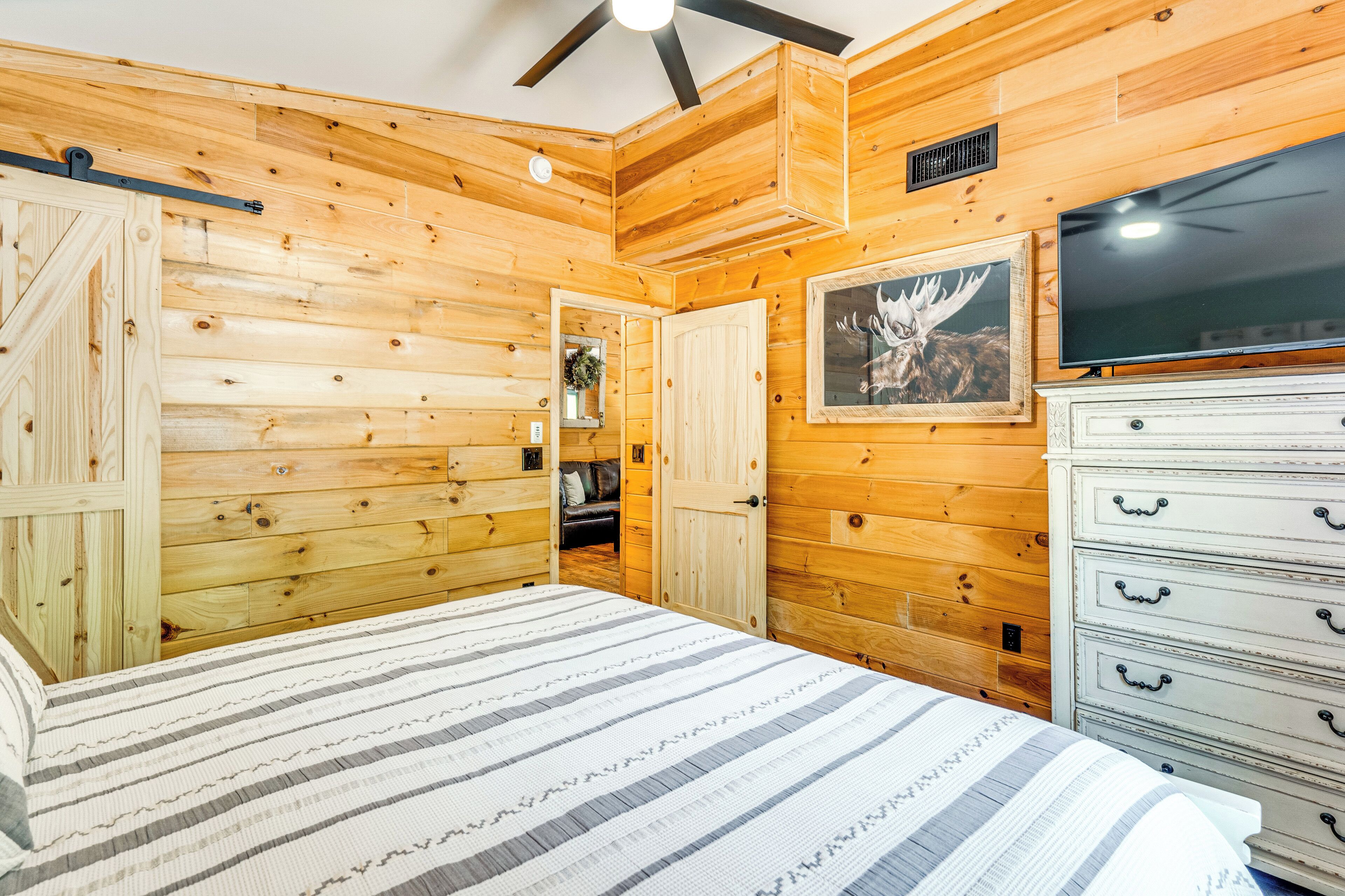 A wooden-paneled room with a bed, dresser, TV, and a door leading to another room.