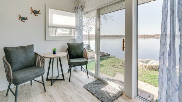 Una habitación con dos sillas, una mesita y vistas a un lago a través de puertas de vidrio amplias.